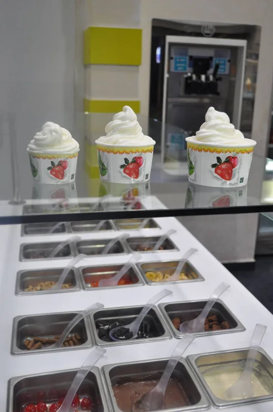 Ο πάγκος με τα toppings και τρία κύπελλα παγωμένο γιαούρτι από πάνω.